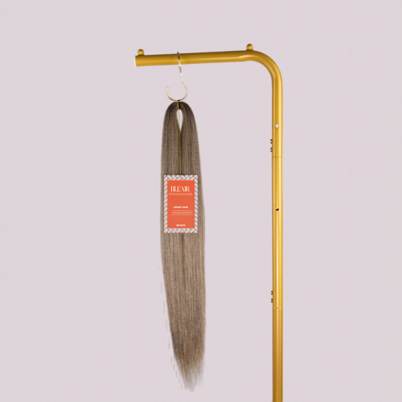 Blhair™ Honey Haze braid hair bundle hanging on gold stand against neutral background.
